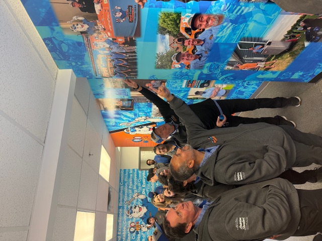 First Care team pointing at their office's picture wall
